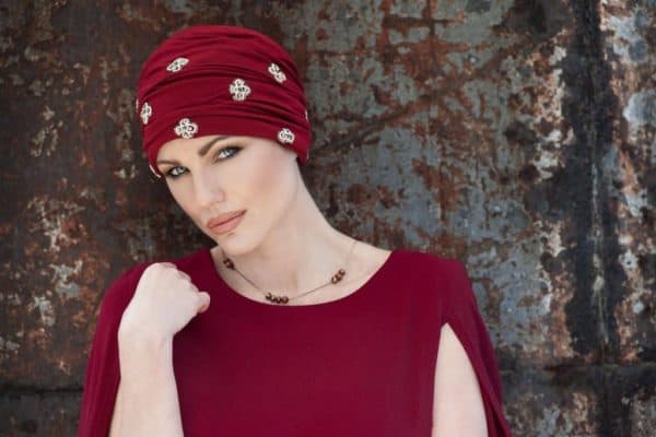 Woman with hair loss wearing a red soft Jewel Hat with white beads.