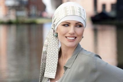 Woman with no hair wearing a white bamboo hat with a flower print scarf around it.
